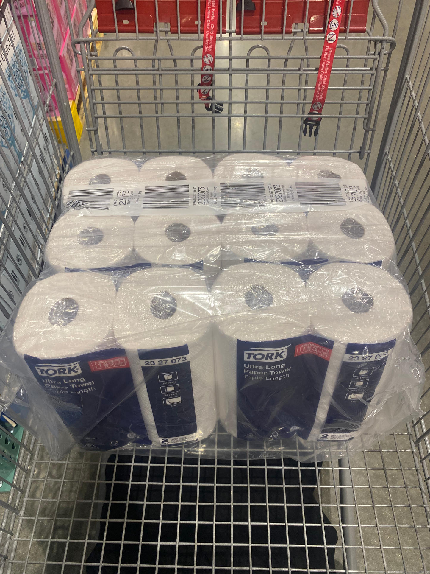 12 paper towels on a shopping cart wrapped on a clear plastic covering with the branded name Tork ultra long paper towel triple length.